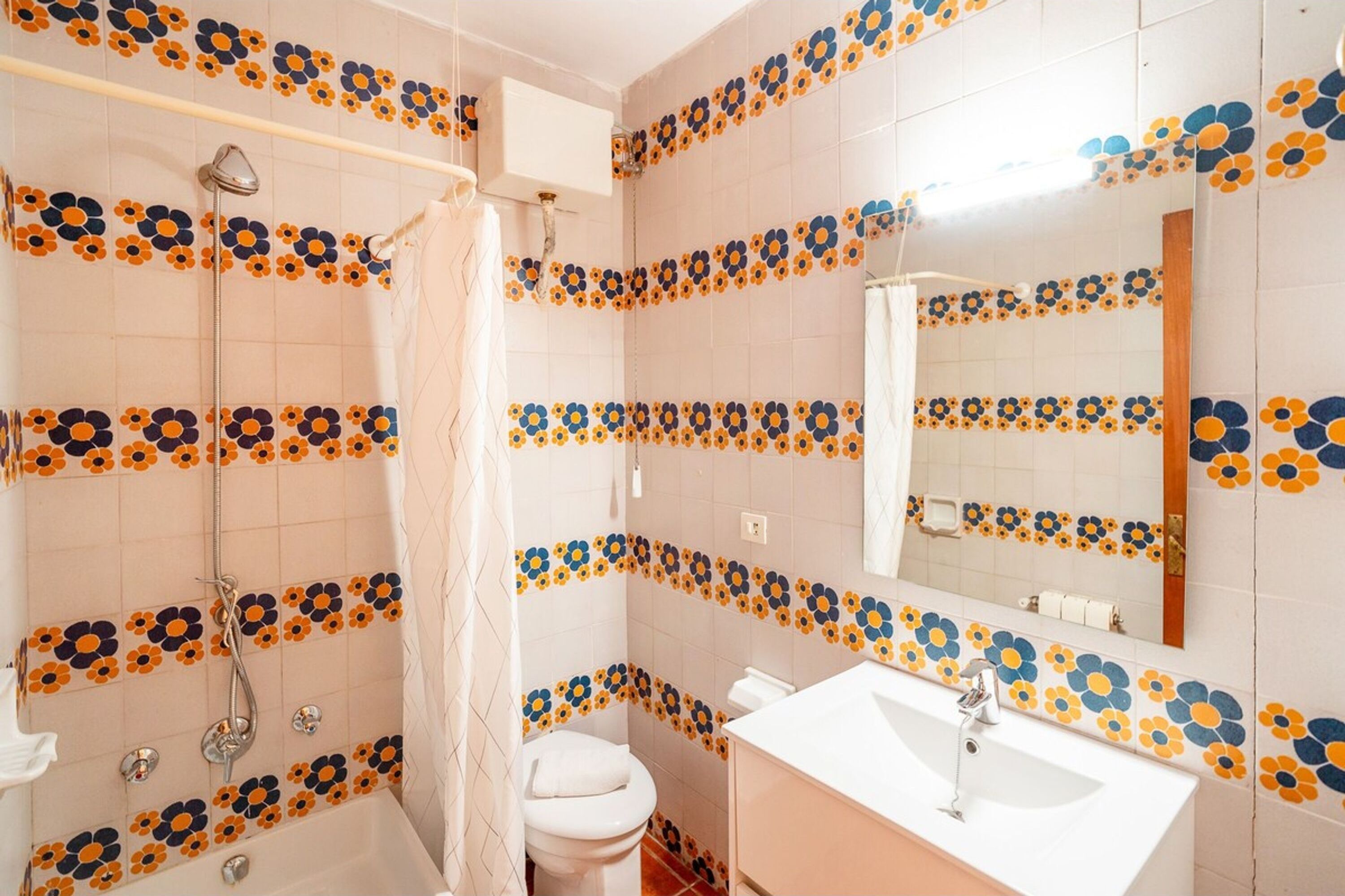Uma casa de banho com chuveiro, sanita, lavatório e espelho.