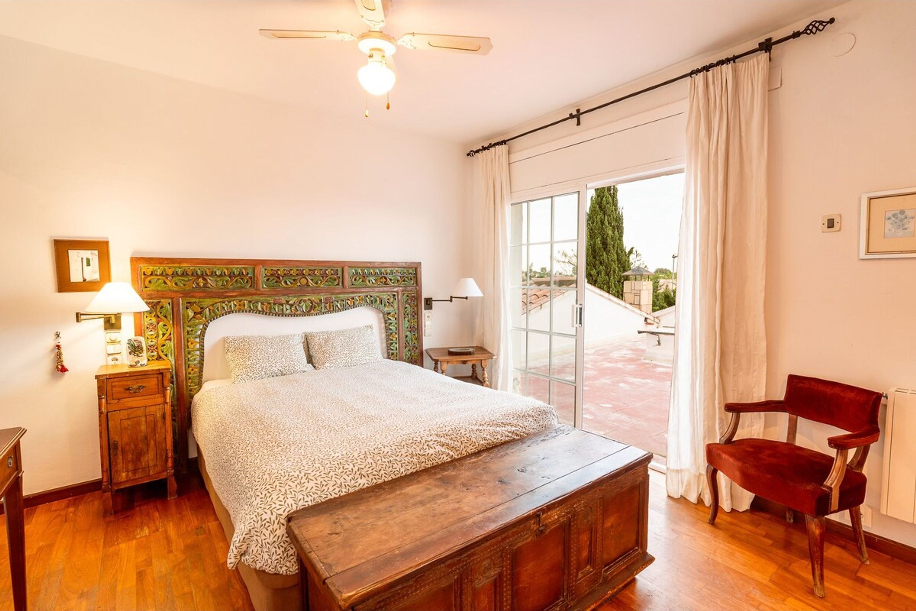 Un dormitorio con cama de madera, mesita de noche, una silla y una ventana con cortinas.