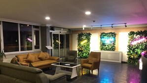 Un salon moderne avec un canapé, des fauteuils et une table basse. De grandes fenêtres et des panneaux muraux décoratifs agrémentent la pièce.