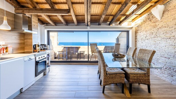 A modern kitchen with a large island, wooden ceiling beams, and a view of the beach. - Unik Vacation Panoramic (Tarragona)