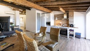 A modern living room with a glass coffee table, wicker chairs, and a sofa. A kitchen with white appliances and wooden cabinets is visible in the background. - Unik Vacation Panoramic (Tarragona)
