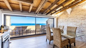 A dining area with wicker chairs and a glass table, overlooking a beach. - Unik Vacation Panoramic (Tarragona)