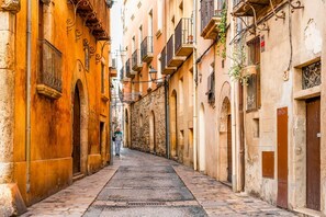 A narrow street lined with buildings featuring stone facades and arched doorways. - Unik Vacation Panoramic (Tarragona)