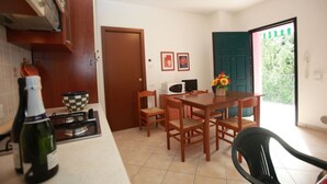 A kitchen with a stove, microwave, and a dining table with chairs. There is a door leading to a balcony with a view of greenery. - Green oasis close to the center (Rosolina Mare)