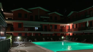 A swimming pool with lounge chairs and a building with balconies in the background. - Green oasis close to the center (Rosolina Mare)