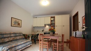 A compact living space with a sofa, a dining table, and chairs, a kitchen area with cabinets and appliances, and a framed picture on the wall. - Green oasis close to the center (Rosolina Mare)