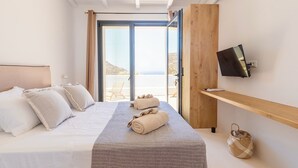 A hotel room with a bed, a TV on the wall, a wooden shelf, and a view of the outdoors.