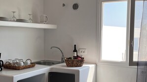 A compact kitchen with a refrigerator, a sink, and a window. - High Point Apartments Fira (Santorini)