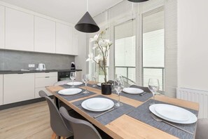 A modern kitchen with white cabinets, a wooden dining table set with white plates and glasses, and a potted orchid on the table.
