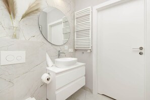A modern bathroom with a white vanity, a round mirror, and a towel rack.