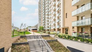 A modern apartment building with multiple balconies, a central courtyard with steps, and surrounding greenery.
