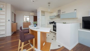 A modern kitchen with a central island, wooden chairs, and a built-in TV.