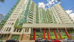 A multi-story hotel with a modern design, featuring a prominent entrance with glass doors and a green and red facade.