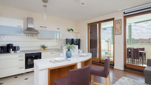 A modern kitchen with white cabinets, a built-in oven, and a dining area with two purple chairs.