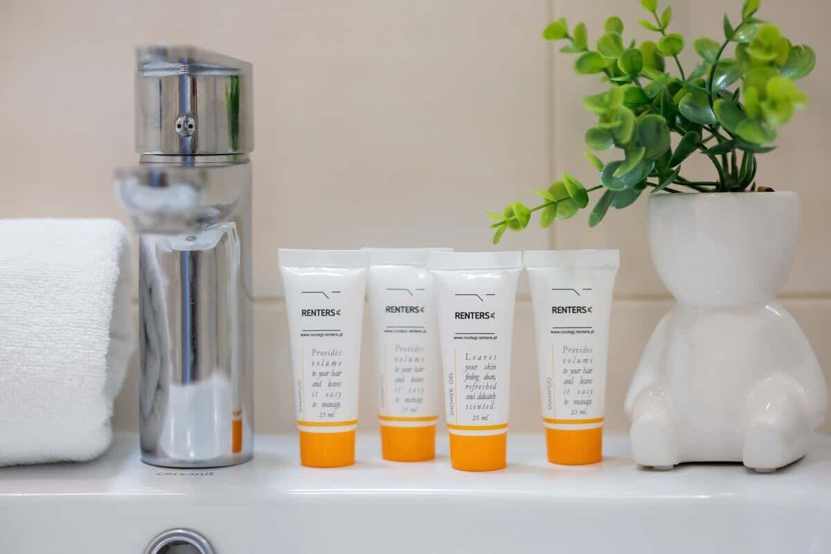 A bathroom shelf with four bottles of RENTERS® body wash, a glass bottle, and a white ceramic figurine.