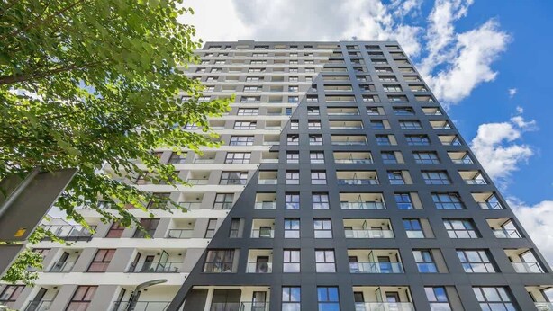 Un edificio moderno de gran altura con varios pisos y balcones, bajo un cielo despejado.