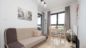 Una sala moderna con un sofá, una mesa de comedor con sillas, un televisor de pantalla plana y una ventana con cortinas.
