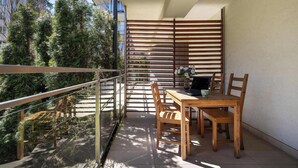 A balcony with a wooden table and chairs, a railing, and a view of trees and buildings. - Spacious Apartment | 3 Bedrooms, Pool, Parking. (Zakopane)