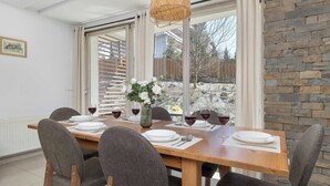 A dining area with a wooden table, grey upholstered chairs, a vase with flowers, and wine glasses. - Spacious Apartment | 3 Bedrooms, Pool, Parking. (Zakopane)