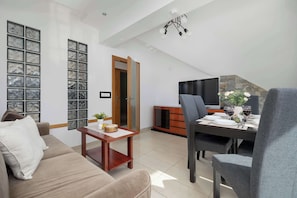 A modern living room with a sofa, a dining table set for four, a TV, and a staircase leading to an upper level. - Elegant Apartment | 3 Bedrooms, Pool and Sauna (Zakopane)