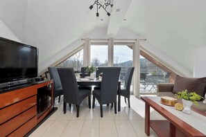 A modern dining area with a TV, dining table, chairs, and a view through large windows.