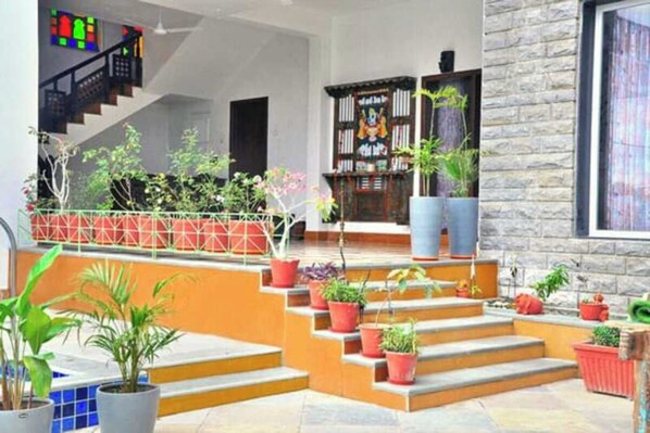 Un interior moderno con una escalera que sube a un segundo piso, rodeado de plantas en macetas y una pared de piedra.