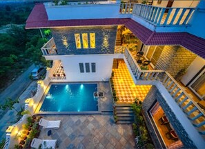 Una casa de dos pisos con piscina, mobiliario exterior y un balcón.