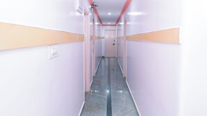 A long, narrow hallway with white walls and a pink ceiling, leading to a door at the end. - Hotel Natasha Regency (Bengaluru)