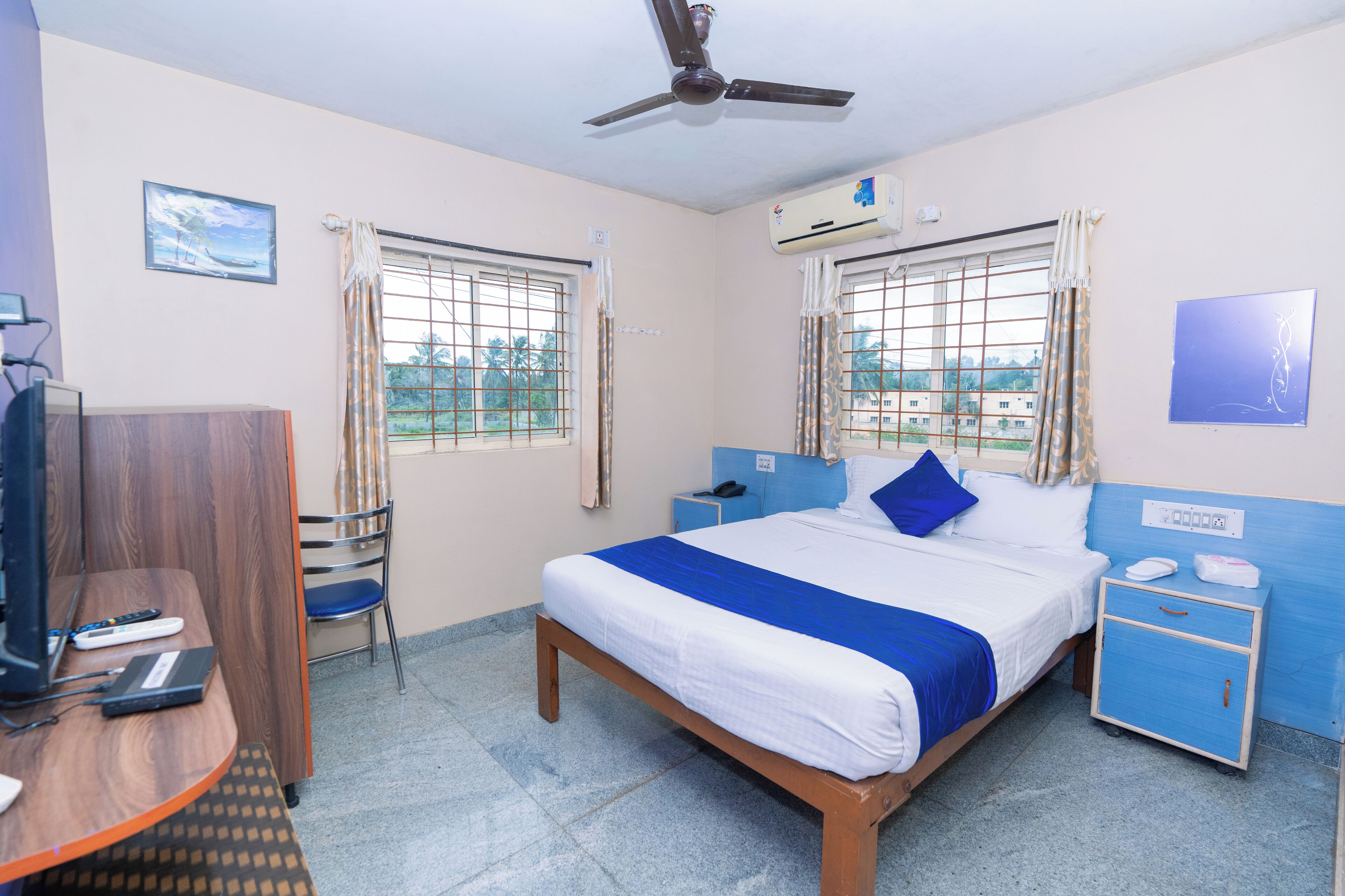 Una habitación de hotel con cama, escritorio, silla, televisor y ventilador de techo.