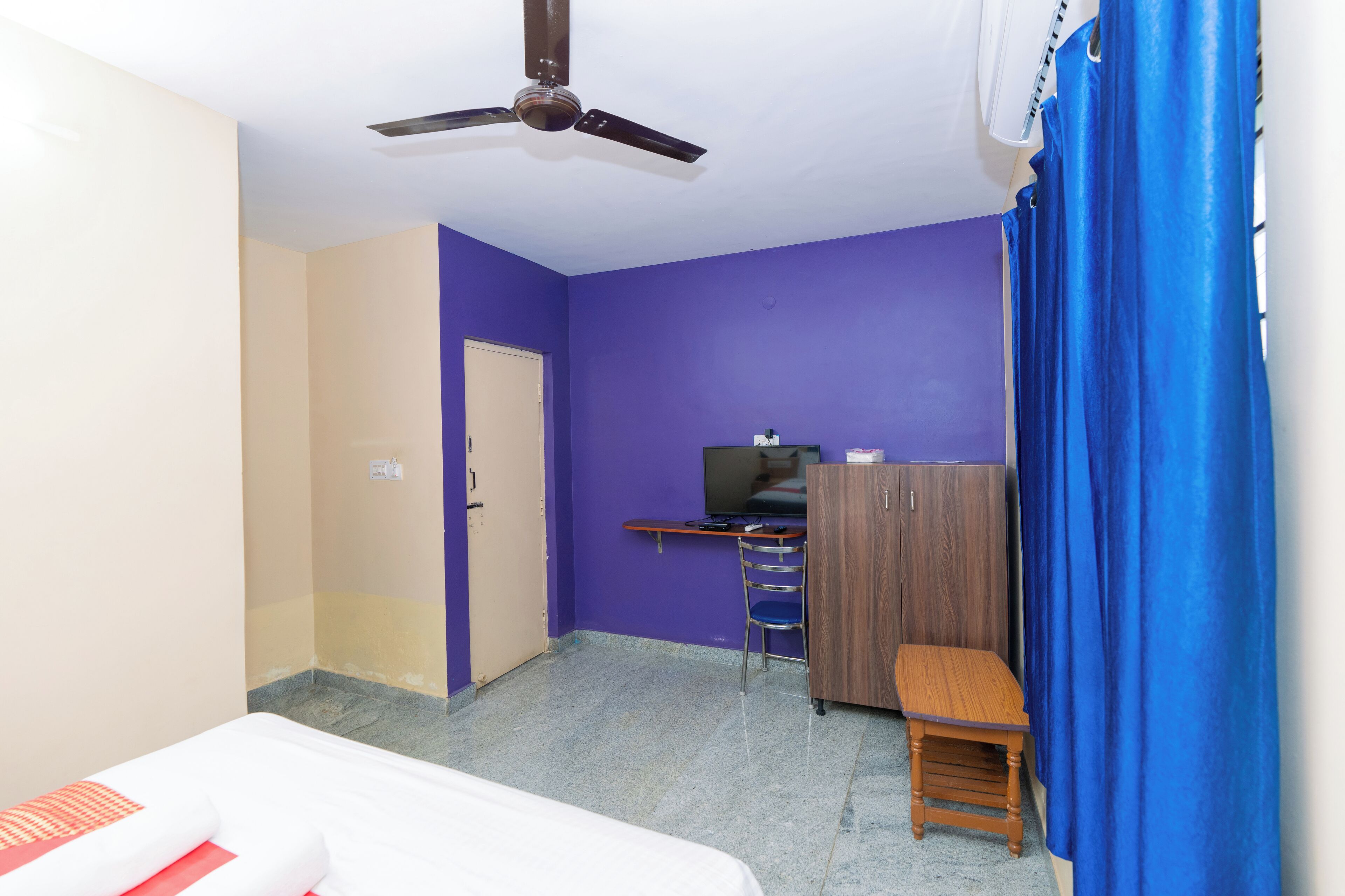 Una habitación con cama, escritorio, silla, televisor y ventilador de techo.