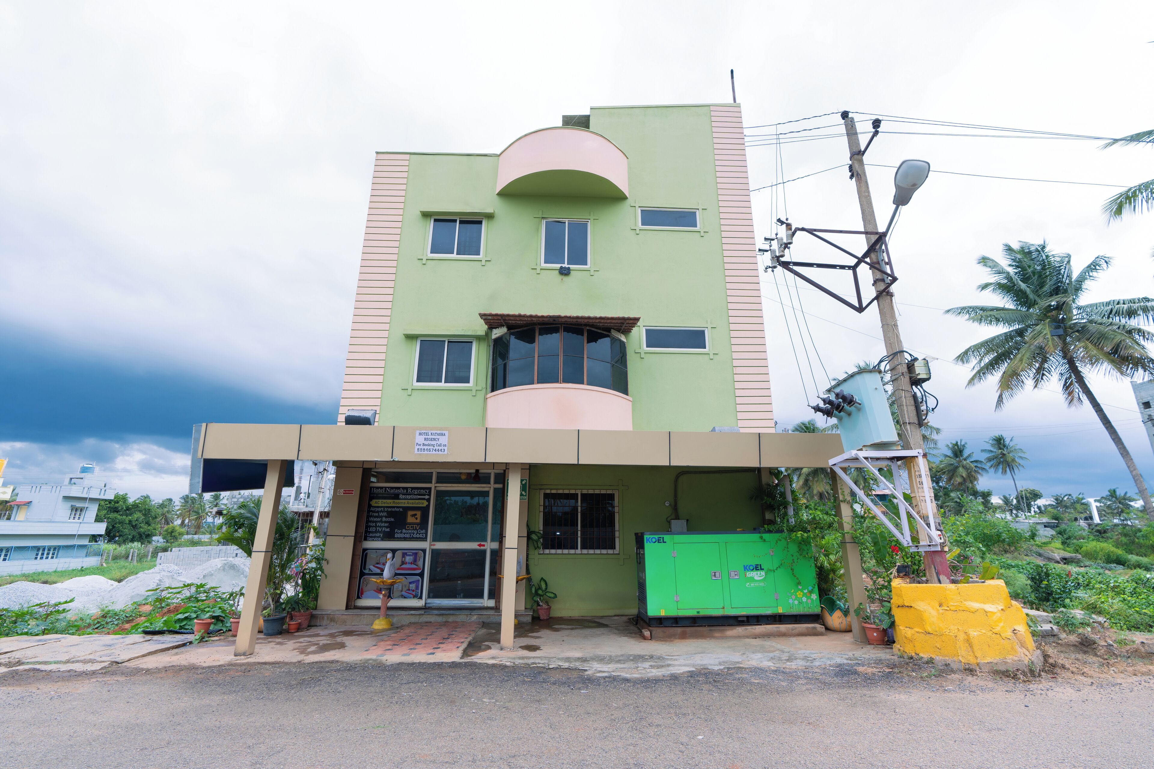 A multi-story building with a green facade, a flat roof, and a small entrance area with a green cabinet and potted plants.
