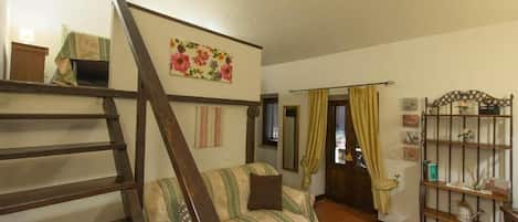 Una habitación acogedora con una escalera de madera, un sofá a rayas, una mesita y una estantería con adornos.