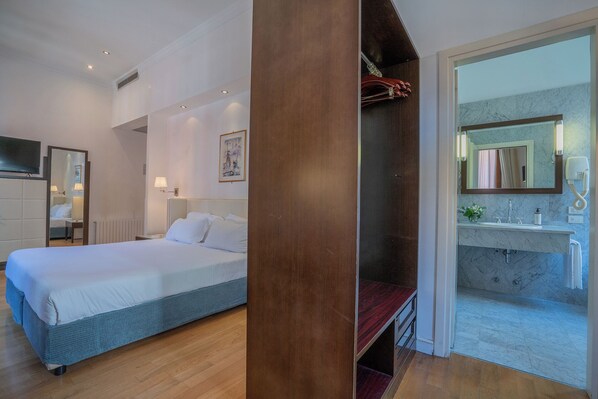 A hotel room with a bed, bedside table, lamp, and a view of the bathroom with a sink and mirror. - Residenza San Marco (Venice)