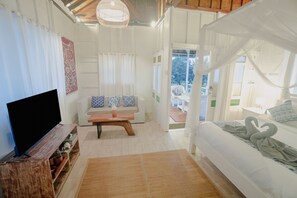 A bedroom with a bed, a TV, a sofa, and a window. - Noya Bed and Breakfast (Ubud)