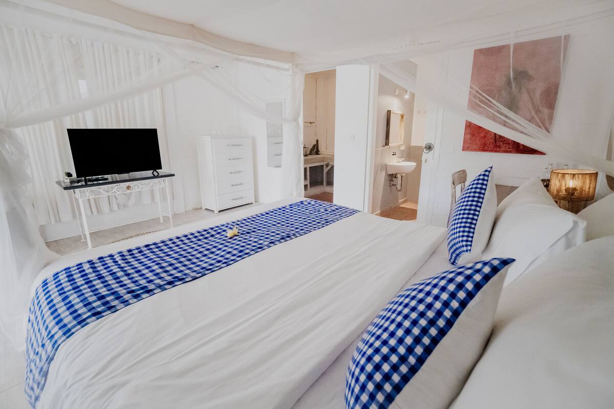 A hotel room with a large bed, a TV, a desk, and a bathroom visible through an open door.