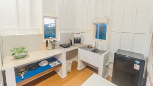A compact kitchen with white cabinetry, a black refrigerator, a sink, and a window with a view of trees. - Noya Bed and Breakfast (Ubud)