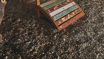 Un banco de madera con un diseño colorido y desgastado, situado sobre grava bajo un árbol.