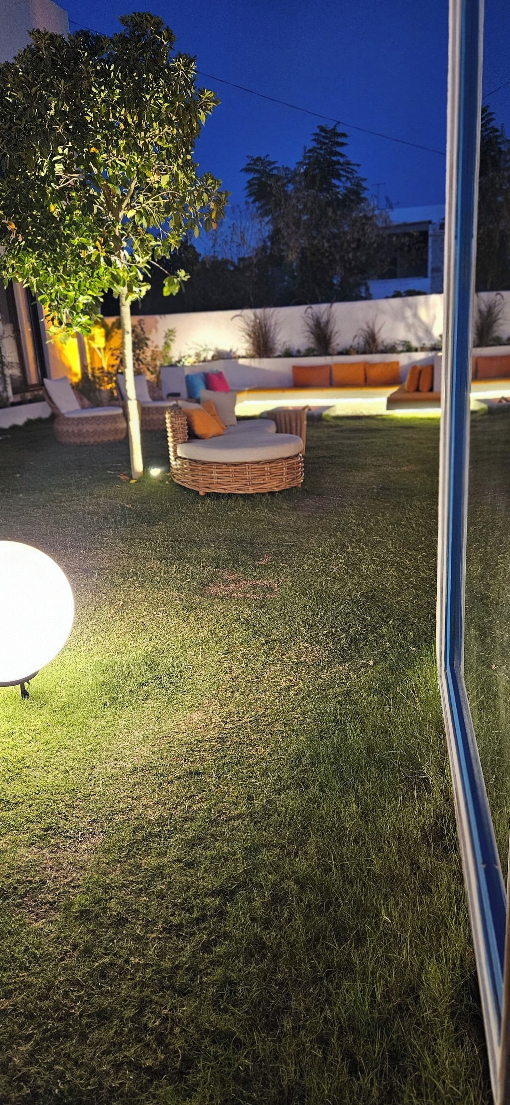 A well-maintained outdoor area with a grassy lawn, a wicker sofa with cushions, and a small tree.
