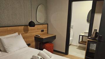 Habitación de hotel con una cama grande, cabecera de madera, mesita de noche con control remoto, una mesita con hervidor y un espejo en la pared.