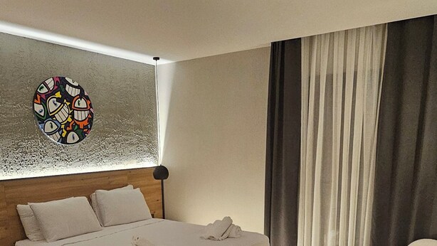 A modern hotel room with a large bed, a bedside table, a lamp, and a view of the city through the window. - Glitz Bodrum (Bodrum)