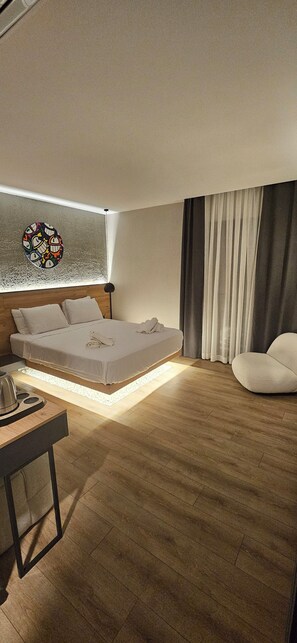 A modern hotel room with a large bed, a bedside table, a lamp, and a view of the city through the window. - Glitz Bodrum (Bodrum)
