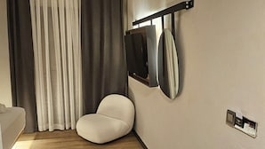 A modern room with a wooden floor, a white bean bag chair, a flat-screen TV mounted on the wall, and a small shelf with items. - Glitz Bodrum (Bodrum)
