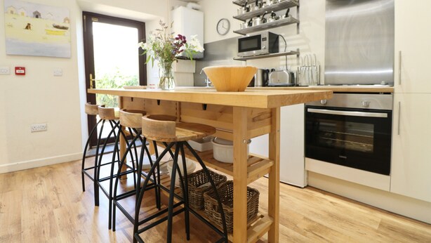Eine moderne Küche mit einer Holztischinsel, Barhocker, einer Mikrowelle, einem Backofen und einer Uhr an der Wand.