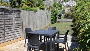 Eine Terrasse mit Tisch und Stühlen, umgeben von einem Holzzaun und üppiger Bepflanzung.