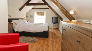 Ein Schlafzimmer mit einem Bett, Holzboden, einem roten Stuhl, einer Kommode und einem Fernseher auf einem kleinen Tisch.