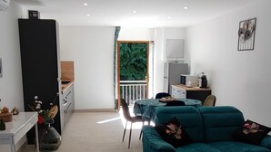 A spacious living room with a teal sofa, a dining area with a green table, and a kitchen area with a black refrigerator.