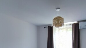 A bedroom with two beds, a bedside table with a lamp, a hanging light fixture, and a window with curtains.