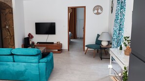 A living room with a teal sofa, a flat-screen TV, a wooden coffee table, and a green chair.
