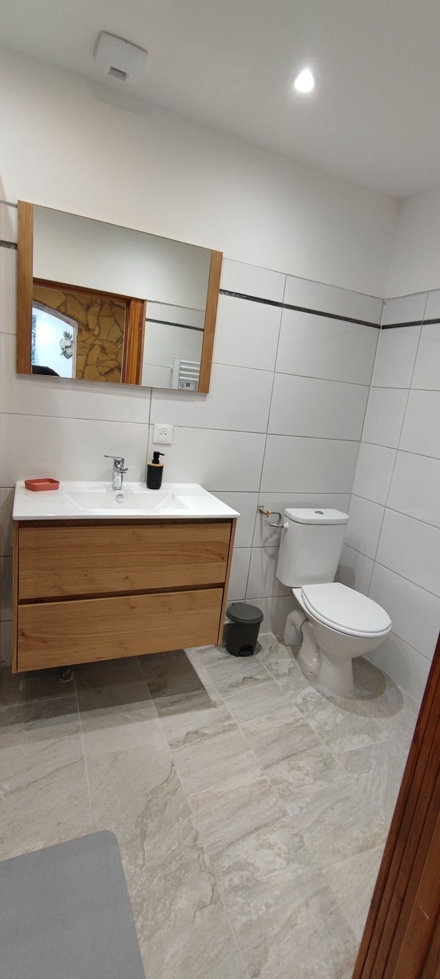 Een badkamer met een wit wastafel, houten wastafelmeubel, spiegel, wit toilet en betegelde wanden.