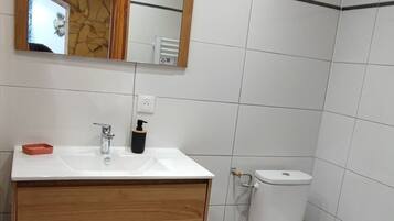 Een badkamer met een wit wastafel, houten wastafelmeubel, spiegel, wit toilet en betegelde wanden.